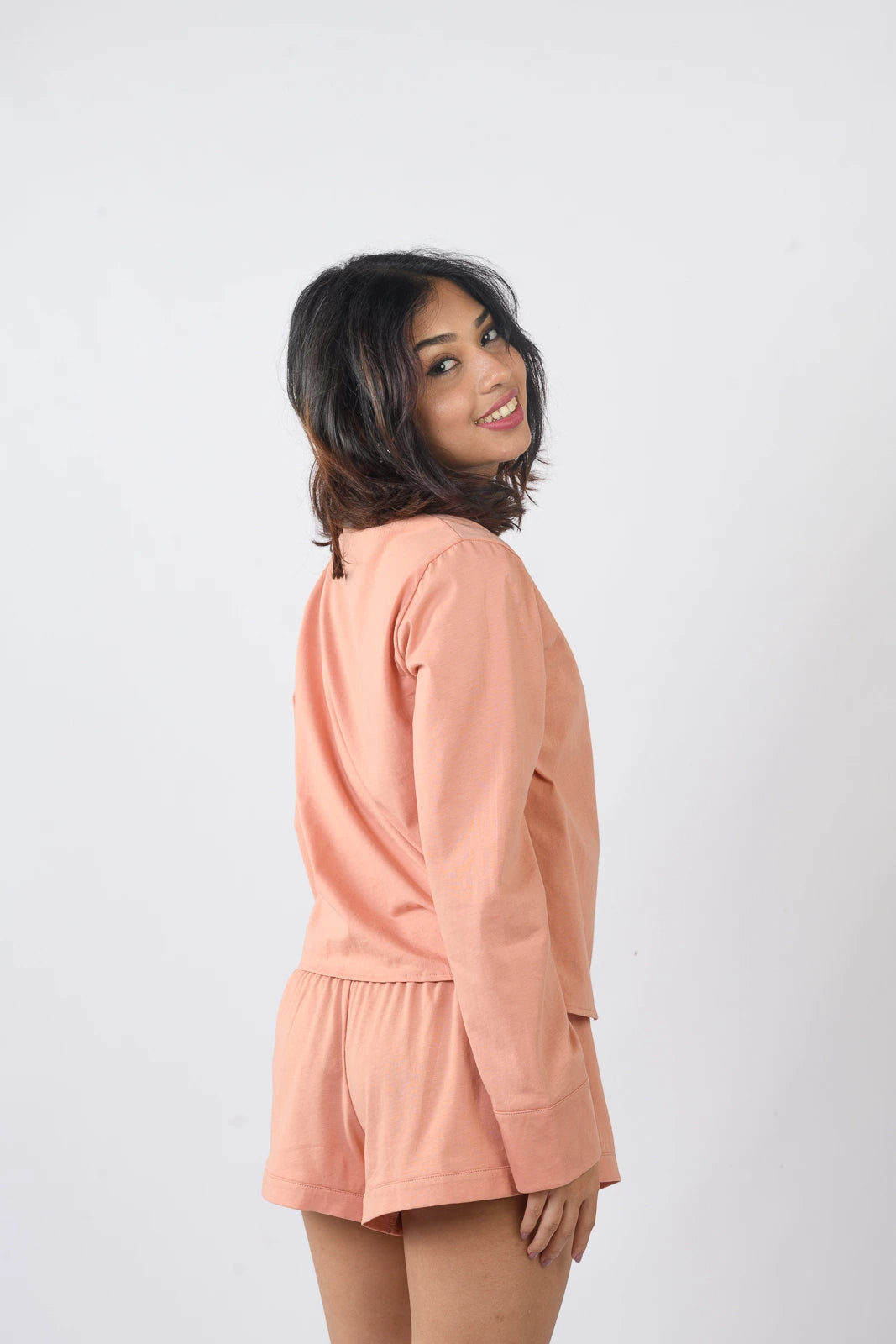 Peach-colored pajama set with a button-up long-sleeve top and matching shorts, styled casually against a white backdrop.