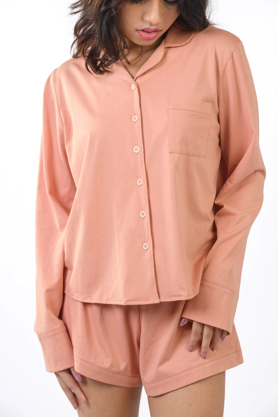 Peach-colored pajama set with a button-up long-sleeve top and matching shorts, styled casually against a white backdrop.