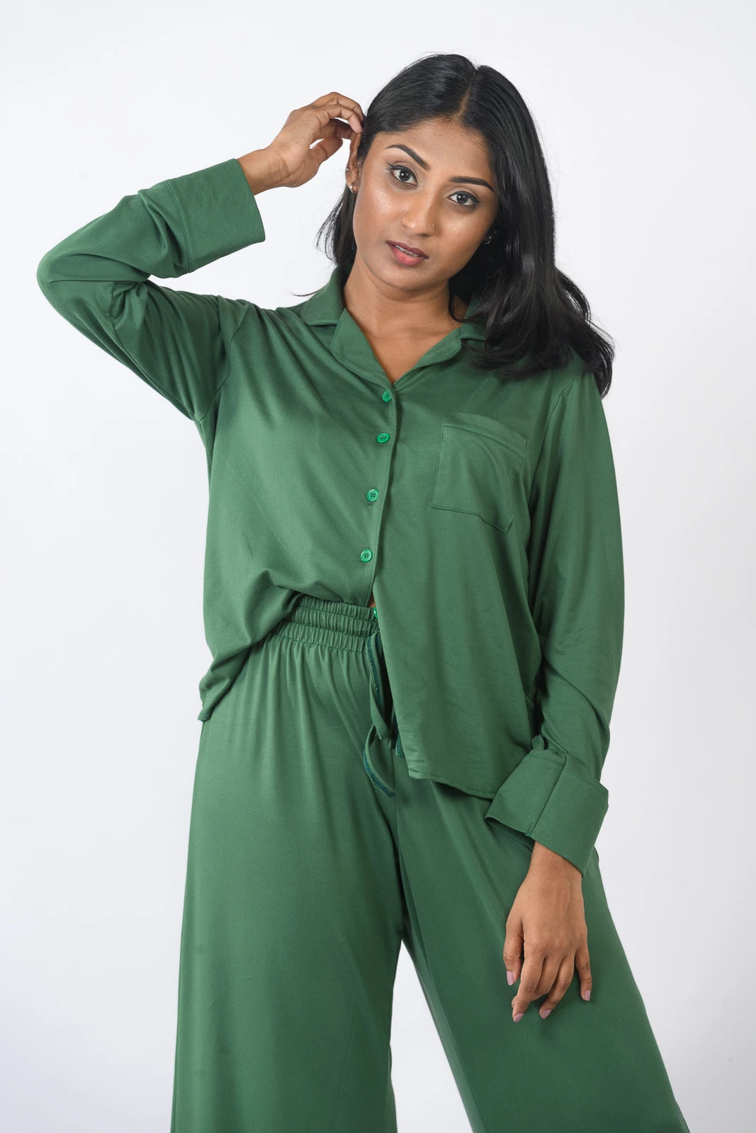 Deep green pajama set with a long-sleeve button-up top and wide-leg pants, presented in a relaxed pose against a plain white background.
