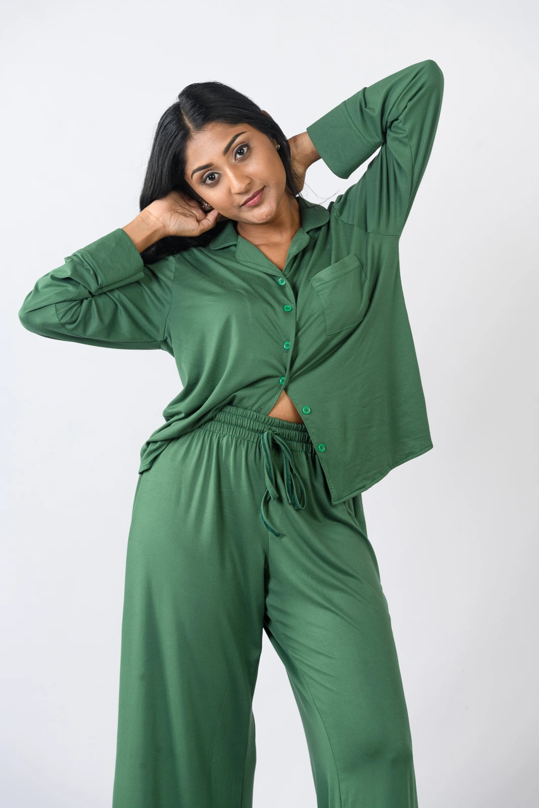 Deep green pajama set with a long-sleeve button-up top and wide-leg pants, presented in a relaxed pose against a plain white background.