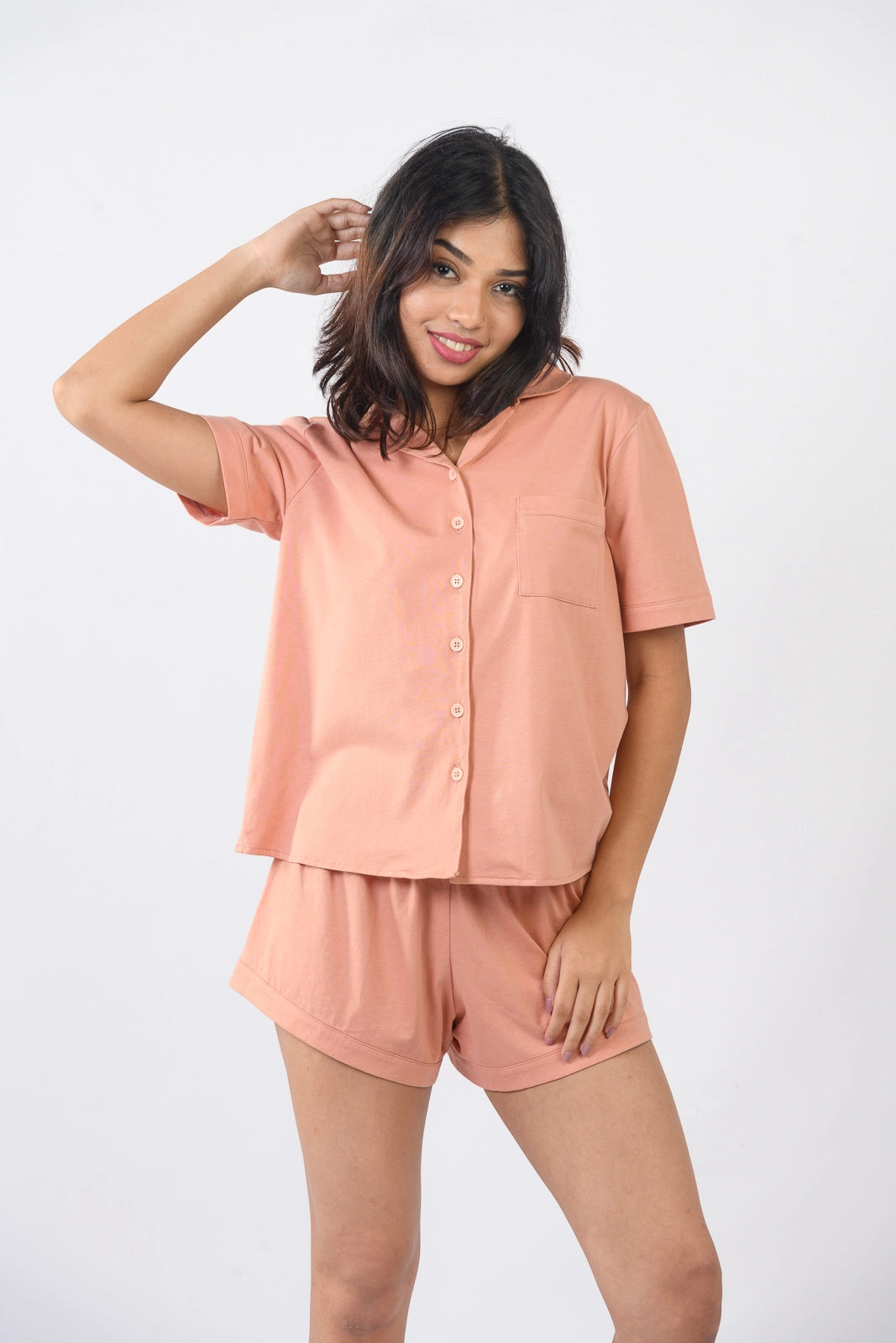 Smiling woman in coral pink sleepwear set posing confidently. Soft, breathable fabric, perfect for cozy sleepwear & stylish relaxation.