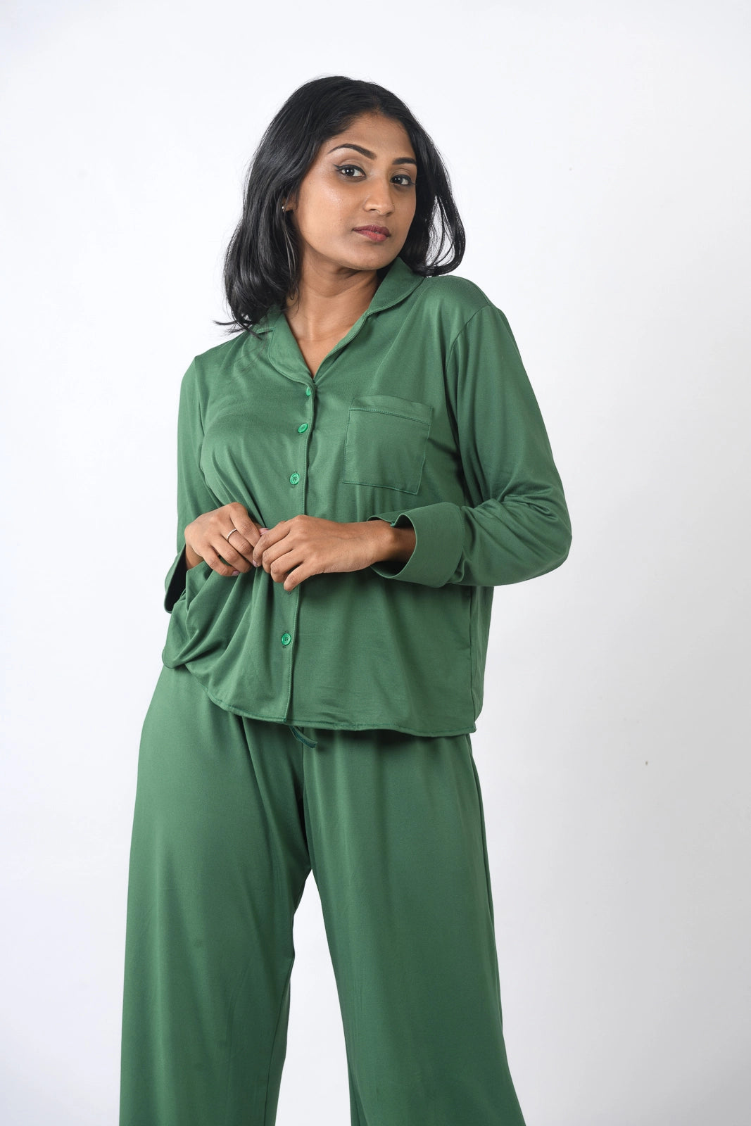 Deep green pajama set with a long-sleeve button-up top and wide-leg pants, presented in a relaxed pose against a plain white background.